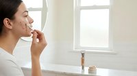 Young woman applying skincare cream in modern bathroom mirror reflection morning routine self-care wellness beauty regimen facial moisturizer.