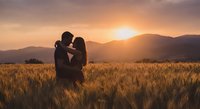 Romantic couple silhouette embracing in golden wheat field at sunset with mountain landscape backdrop for love and relationship concepts.