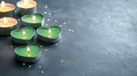 Green tea light candles burning on dark surface with scattered white pearls creating peaceful spa atmosphere for relaxation and wellness rituals.