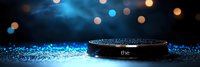Smart speaker device on dark surface with scattered blue glitter and blurred bokeh lights creating magical atmosphere for technology advertising.