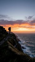 Hiker with backpack standing on rocky cliff overlooking ocean at sunset, golden sky reflecting on water below, adventure and exploration concept for travel and outdoor activities.