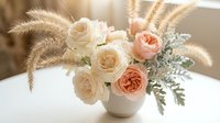 Elegant floral arrangement with cream and peach roses, pampas grass and dusty miller in white vase on marble surface for wedding decor and home styling.