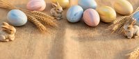 Pastel colored Easter eggs with wheat stalks and wooden bunnies arranged on rustic burlap background for spring holiday celebration and seasonal decorating.
