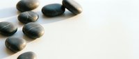 Smooth dark stones arranged on white surface with soft shadows, suitable for wellness, spa, and meditation design projects.