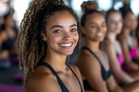 Happy mixed-race woman with curly hair smiling during fitness class with diverse group of women exercising together in bright gym studio.