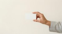 Male hand holding blank white business card against neutral beige background, suitable for corporate branding, marketing mockups, and professional identity design projects.