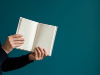 Person with medium skin tone wearing dark business attire holding open blank notebook against teal background, suitable for education, publishing, and corporate communications.