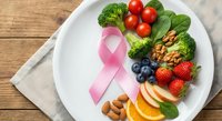 Pink ribbon with healthy foods on white plate including broccoli, berries, nuts and fruits for cancer awareness and prevention diet concept.