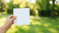 Hand holding blank white card outdoors with green blurred garden background, suitable for mockups, advertising, and promotional designs.