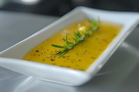 Creamy butternut squash soup garnished with fresh rosemary and black sesame seeds served in modern white rectangular plate, selective focus on herbs.