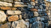 Ancient stone wall with weathered rocks in natural earth tones creating rustic texture for architectural and construction backgrounds.