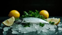 Fresh raw seabass on crushed ice with bright yellow lemons and green parsley garnish against dark background, dramatic food photography for restaurant menu.