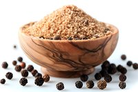 Ground black pepper in wooden olive bowl with scattered whole peppercorns on white background. Natural spice and seasoning ingredient for cooking.