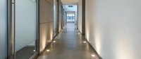 Modern office corridor with glass walls and polished concrete floors featuring LED lighting for contemporary workplace interior design.