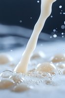 Fresh milk stream pouring with splashes and bubbles creating dynamic motion on light surface, macro photography capturing liquid movement and texture.