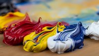 Colorful acrylic paint strokes in red, yellow, blue and white on wooden palette creating vibrant artistic composition for creative projects and art supplies.