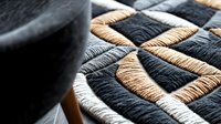 Macro view of woven textile pattern in black, beige and white threads creating geometric design. Detailed close-up shows texture and craftsmanship of fabric weaving.
