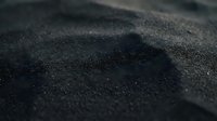 Close-up macro view of fine black sand grains with shallow depth of field creating abstract textural patterns for backgrounds and design projects.