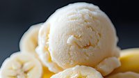 Creamy vanilla ice cream scoop with fresh banana slices on dark background, soft focus macro shot highlighting smooth texture and natural ingredients.