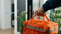 Person carrying bright orange emergency preparedness bag with reflective strips at home entrance for disaster readiness and safety planning.