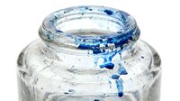 Closeup of clear glass jar with blue paint splatter and drips on rim, suitable for art, craft, and creative projects.