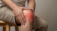 Senior man holding inflamed knee showing arthritis pain and joint discomfort while sitting on wooden stool in medical healthcare concept.