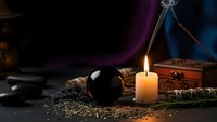 Mystical fortune telling setup with crystal ball, burning candle, tarot cards and dried herbs on dark wooden table for divination and spiritual practices.