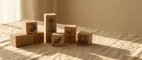 Wooden blocks with engraved symbols including hearts, leaves, and decorative patterns arranged on surface with natural sunlight shadows for crafting projects.