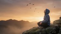 Young woman meditating on mountain cliff at sunrise with birds flying overhead, peaceful mindfulness practice in nature for wellness and spiritual growth.