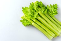 Fresh green celery stalks with leaves arranged on white background, raw organic produce for healthy eating and cooking. Isolated food photography.