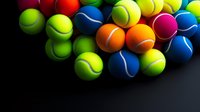 Colorful tennis balls scattered on dark background creating vibrant sports composition. Multiple neon yellow, blue, red, orange and pink balls with dynamic lighting.