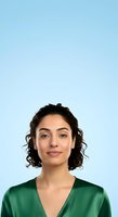 Young woman with shoulder-length curly dark hair and olive complexion wearing green v-neck top against light blue background for professional headshot or corporate portrait use.