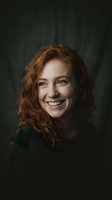 Happy young Caucasian woman with curly red hair smiling warmly in cozy green sweater against dark emerald background for lifestyle and portrait photography.