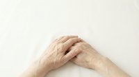 Elderly hands clasped together showing wrinkled skin and aging signs on neutral background for healthcare and senior care concepts.