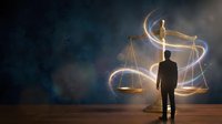Businessman silhouette standing before glowing scales of justice with light trails against starry cosmic background representing legal decisions and balance.