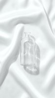 Empty glass bottle on white silk fabric with soft shadows, suitable for cosmetics, skincare, perfume, and luxury product packaging mockups.