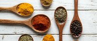 Colorful spices and herbs in wooden spoons on rustic white background. Turmeric, paprika, oregano, black pepper arranged for cooking and seasoning culinary ingredients.