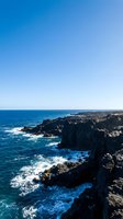 Dramatic rocky coastal cliffs with crashing waves and clear blue sky, perfect for travel, nature, and tourism marketing materials.