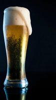 Fresh beer glass with golden lager and white foam head on dark background. Cold alcoholic beverage with bubbles and condensation for bar and restaurant use.