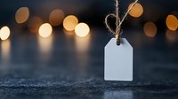 Empty white paper tag hanging on rustic twine string against dark background with soft golden bokeh lights creating magical holiday atmosphere.