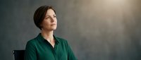 Professional middle-aged Caucasian businesswoman in emerald green blouse looking upward with confident expression against soft gradient background for corporate content.