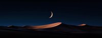Crescent moon illuminating desert sand dunes at twilight, dramatic panoramic landscape with dark blue sky and golden sand ridges in moonlight.
