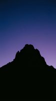 Mountain silhouette against twilight sky with purple and blue gradient, stars visible overhead. Dramatic landscape for nature, travel, and inspirational design projects.