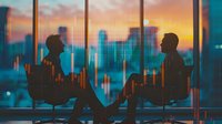 Silhouettes of business professionals in discussion against city skyline and sunset, with financial market data overlay creating dramatic urban atmosphere.