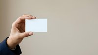 Male hand holding blank white business card against neutral beige background, suitable for corporate branding, identity design, and marketing presentations.