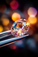 Brilliant cut diamond held by tweezers against blurred bokeh background with warm orange and pink lights, showcasing luxury jewelry craftsmanship and sparkle.