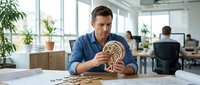 Caucasian businessman assembling wooden mechanical puzzle at modern office desk during break time for stress relief and mental stimulation.