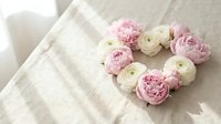 Heart-shaped arrangement of pink and white ranunculus flowers on soft linen fabric. Romantic floral composition for wedding, Valentine's Day, love concepts.