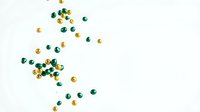 Scattered green and gold beads on white background creating elegant jewelry making supplies pattern for craft projects and creative designs.