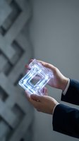 Businessperson holding glowing neon square geometric shape with purple and blue light against modern gray background. Technology and innovation concept.